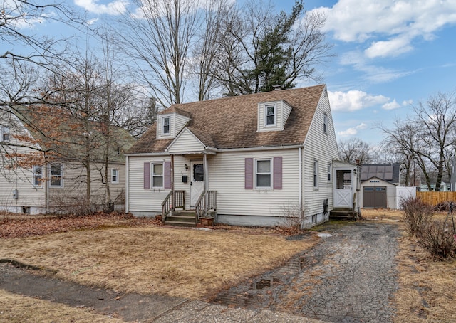 new england style home featuring a shingled roof, driveway, and fence