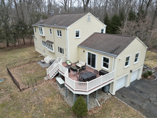 rear view of property featuring a garage, driveway, a chimney, roof with shingles, and a wooden deck