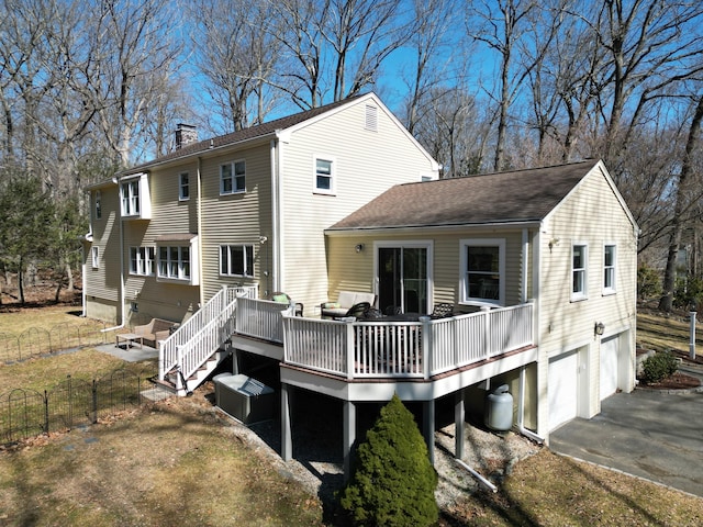 back of property featuring fence, driveway, a wooden deck, an attached garage, and a chimney
