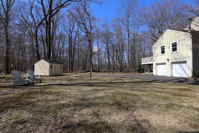 view of yard featuring a storage unit, an outbuilding, an attached garage, and driveway