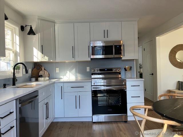 kitchen featuring dark wood-style flooring, stainless steel appliances, light countertops, white cabinetry, and a sink