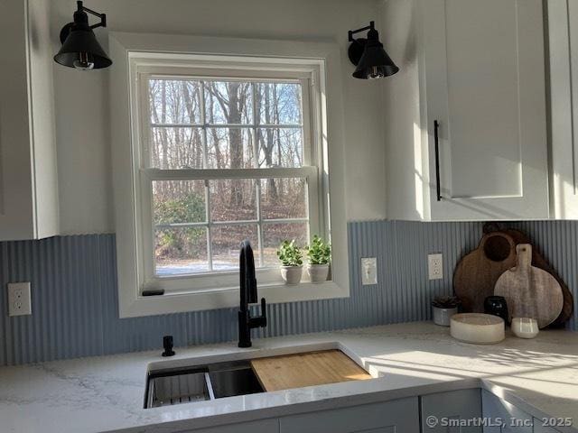 kitchen featuring a sink, light stone countertops, and white cabinets