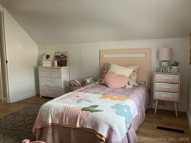 bedroom with visible vents, vaulted ceiling, baseboards, and wood finished floors