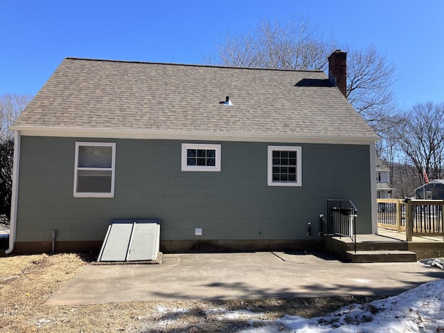 rear view of house with roof with shingles and a chimney