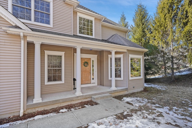 snow covered property entrance featuring a shingled roof and a porch