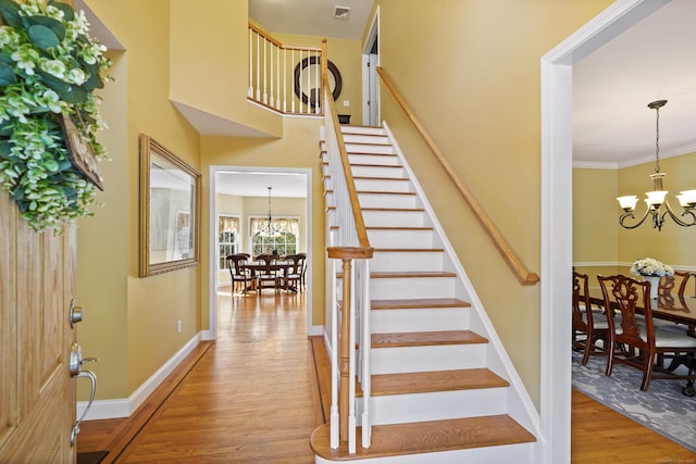 stairway featuring an inviting chandelier, baseboards, wood finished floors, and ornamental molding