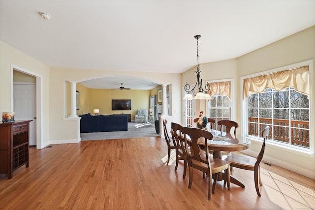 dining room featuring arched walkways, light wood finished floors, baseboards, and ornate columns