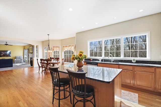 kitchen featuring arched walkways, a breakfast bar area, stainless steel dishwasher, light wood-type flooring, and a center island