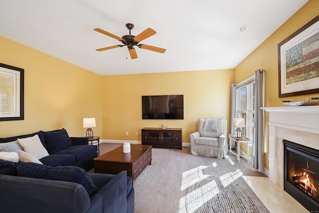 living area with baseboards, a premium fireplace, a ceiling fan, and light colored carpet