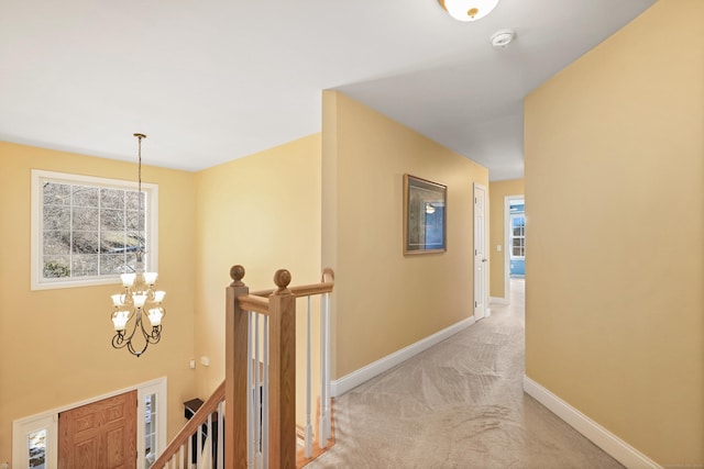 hallway featuring a chandelier, light colored carpet, plenty of natural light, and baseboards