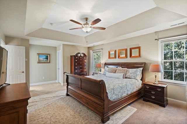 bedroom with light carpet, a ceiling fan, visible vents, baseboards, and a tray ceiling