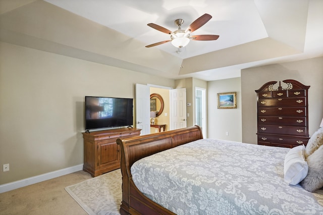 bedroom with light carpet, baseboards, a raised ceiling, and a ceiling fan