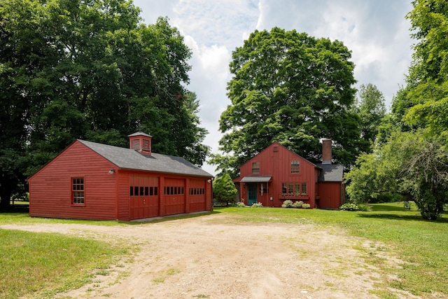 exterior space with an outbuilding, a garage, dirt driveway, a yard, and a chimney