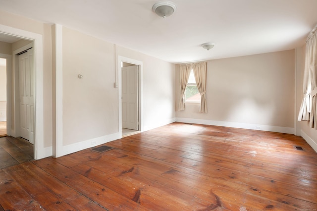 unfurnished room featuring baseboards, visible vents, and hardwood / wood-style floors