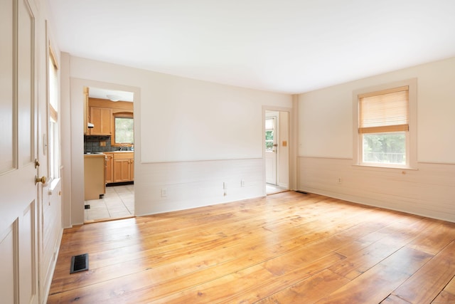 empty room featuring light wood-style flooring, visible vents, a sink, and wainscoting