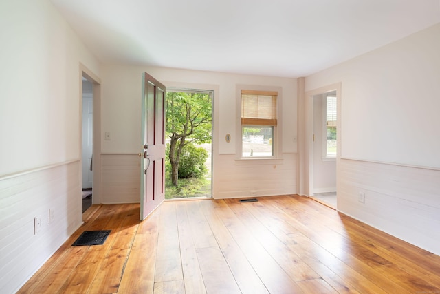 doorway to outside featuring light wood-type flooring, a wainscoted wall, and visible vents