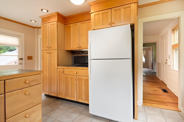 kitchen with crown molding, light tile patterned floors, light countertops, light brown cabinetry, and freestanding refrigerator