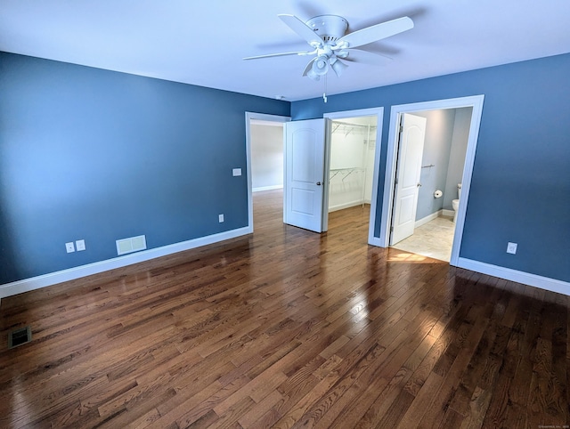 unfurnished bedroom featuring visible vents, a spacious closet, baseboards, and wood finished floors