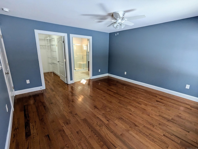 unfurnished bedroom featuring a ceiling fan, baseboards, a closet, dark wood-style floors, and a walk in closet