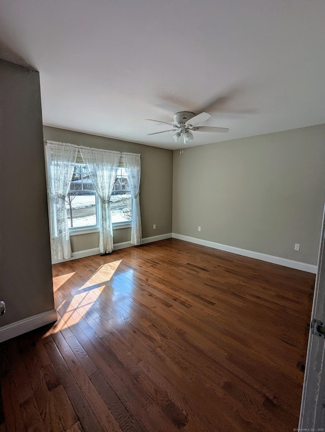 spare room with dark wood-type flooring, ceiling fan, and baseboards