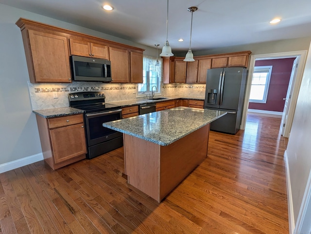 kitchen featuring a sink, wood finished floors, a kitchen island, appliances with stainless steel finishes, and dark stone counters