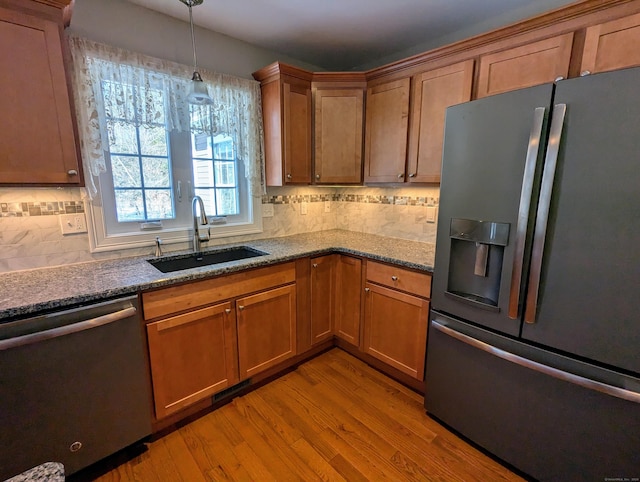 kitchen with brown cabinets, decorative light fixtures, appliances with stainless steel finishes, a sink, and light wood-type flooring