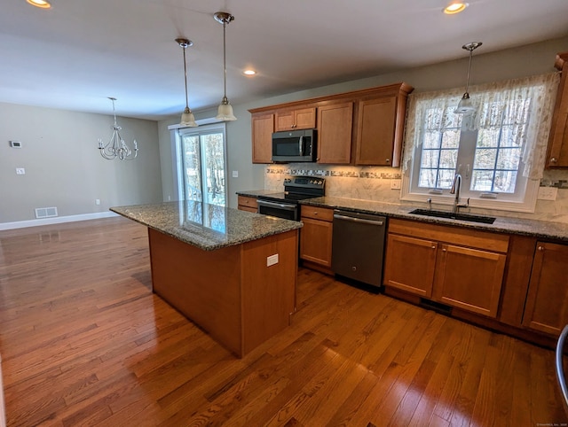 kitchen featuring stainless steel appliances, a sink, a center island, brown cabinetry, and pendant lighting