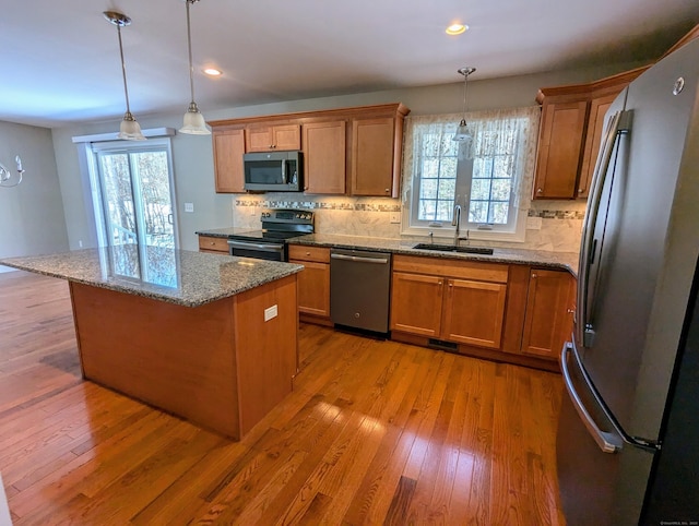 kitchen with brown cabinets, pendant lighting, stainless steel appliances, and a sink