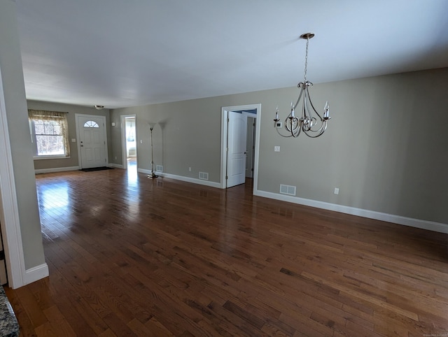 unfurnished living room with a chandelier, dark wood finished floors, visible vents, and baseboards