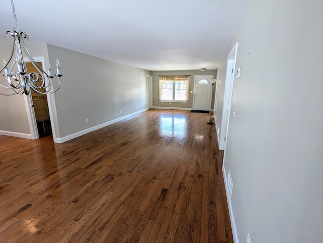 unfurnished living room featuring dark wood-type flooring, a chandelier, and baseboards