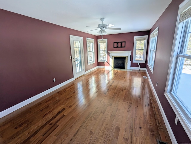 unfurnished living room featuring ceiling fan, a fireplace with flush hearth, visible vents, baseboards, and light wood-style floors