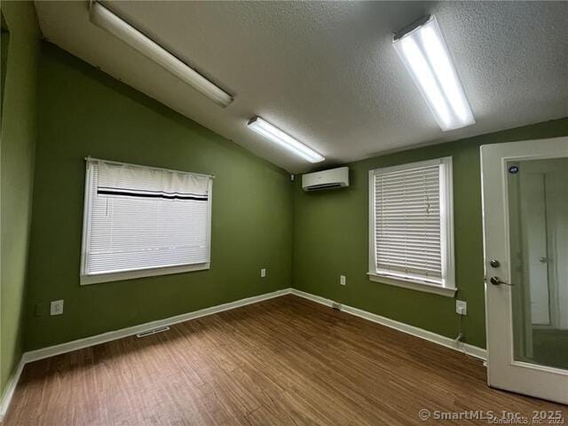 empty room featuring visible vents, lofted ceiling, wood finished floors, a wall mounted air conditioner, and a textured ceiling