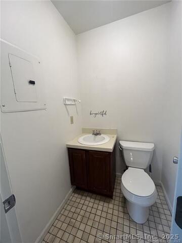 half bath featuring toilet, electric panel, baseboards, and vanity