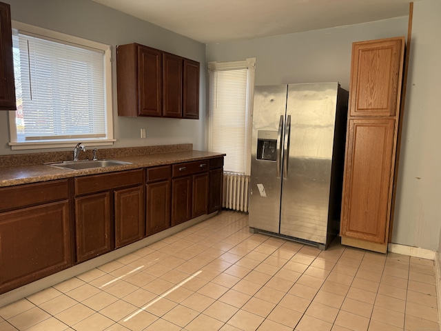 kitchen featuring light tile patterned floors, dark countertops, radiator heating unit, a sink, and stainless steel fridge