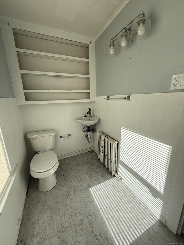 half bath with toilet, radiator heating unit, built in shelves, and a sink