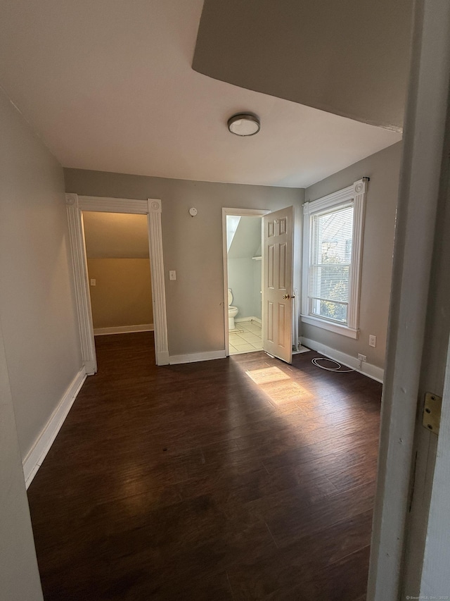 unfurnished bedroom with connected bathroom, baseboards, and wood finished floors