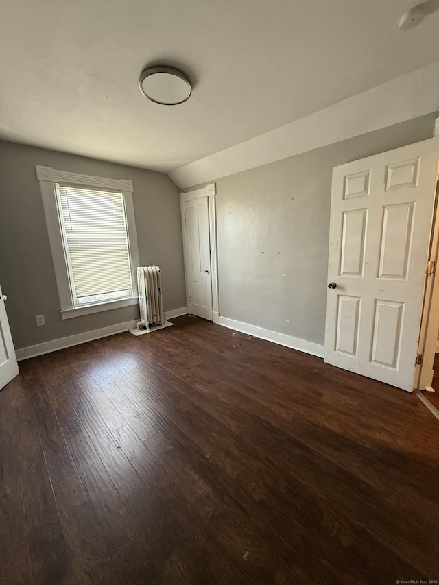 unfurnished bedroom with radiator, dark wood-style floors, baseboards, and vaulted ceiling