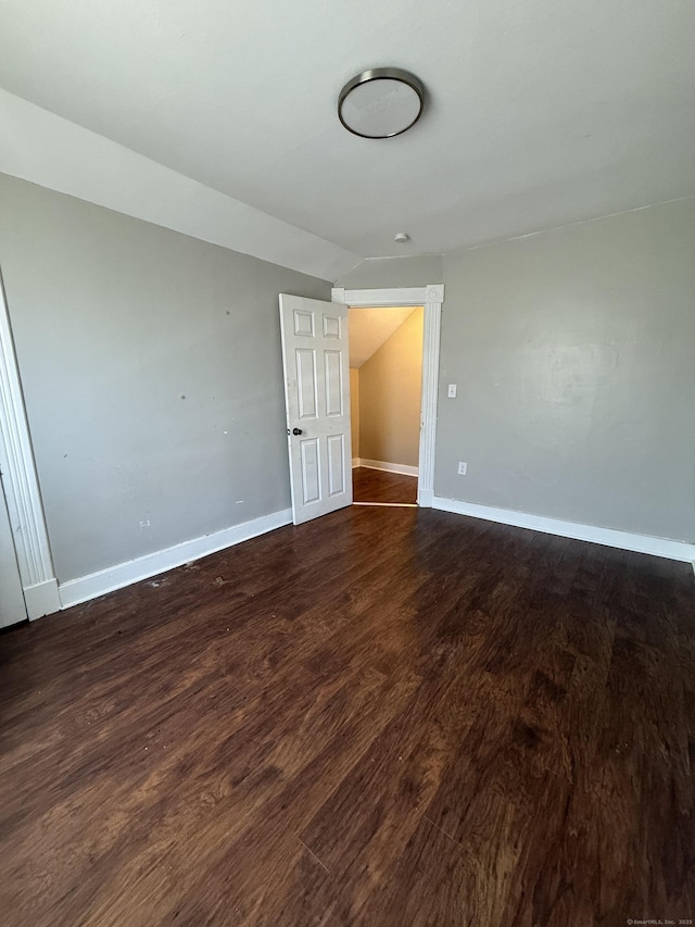 empty room featuring lofted ceiling, baseboards, and wood finished floors