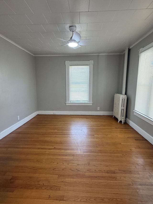 empty room featuring ornamental molding, radiator heating unit, wood finished floors, and baseboards