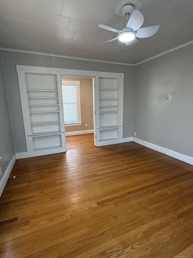 unfurnished room with built in features, crown molding, baseboards, and wood finished floors