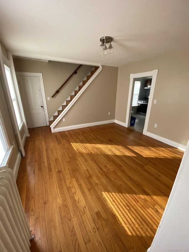 unfurnished living room with baseboards, stairway, and hardwood / wood-style floors