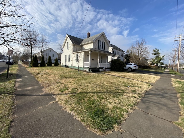 view of side of property with covered porch, a chimney, and a lawn