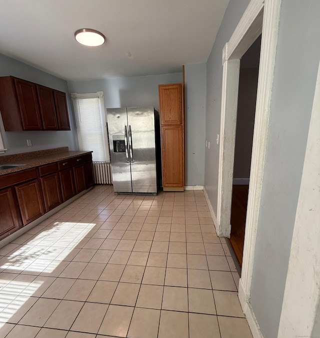 kitchen with light tile patterned floors, a sink, stainless steel fridge, and baseboards