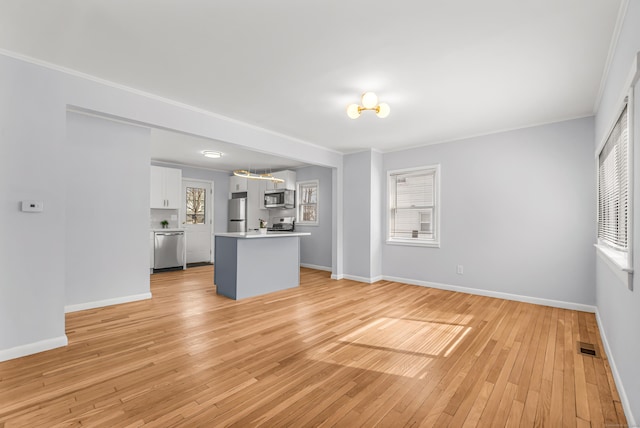 unfurnished living room with light wood-type flooring, a healthy amount of sunlight, and baseboards