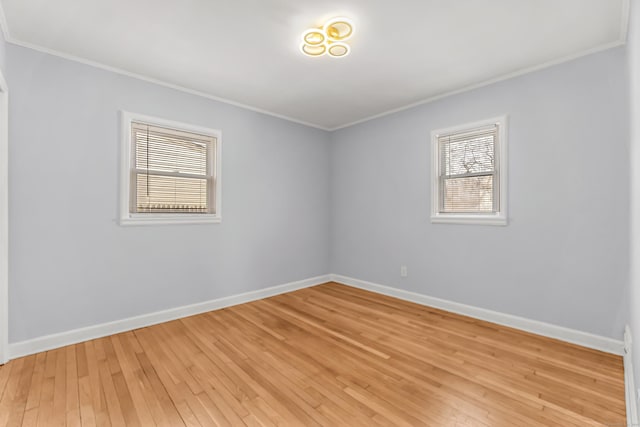 empty room with ornamental molding, light wood-style flooring, and baseboards