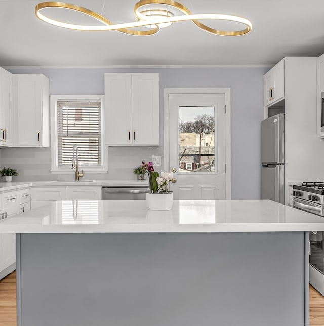 kitchen featuring stainless steel appliances, a sink, white cabinets, light countertops, and ornamental molding