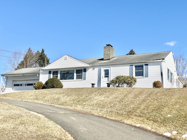 ranch-style home with an attached garage, a chimney, and a front yard