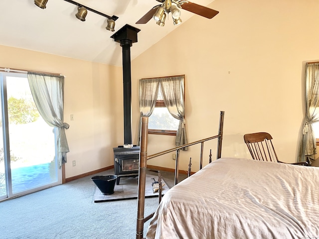 carpeted bedroom with a wood stove, vaulted ceiling, ceiling fan, access to outside, and baseboards