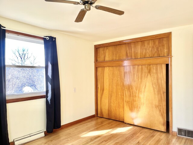 unfurnished bedroom with ceiling fan, a baseboard radiator, light wood-style flooring, visible vents, and baseboards