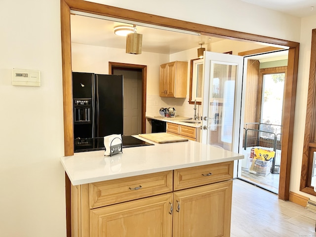 kitchen featuring light brown cabinets, a kitchen island, light countertops, black appliances, and tasteful backsplash